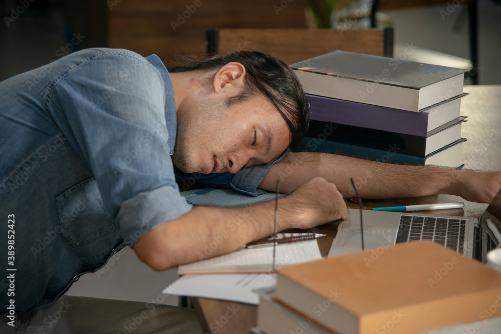 Researcher napping with stack of book and laptop in front of him Researcher napping with stack of book and laptop in front of him