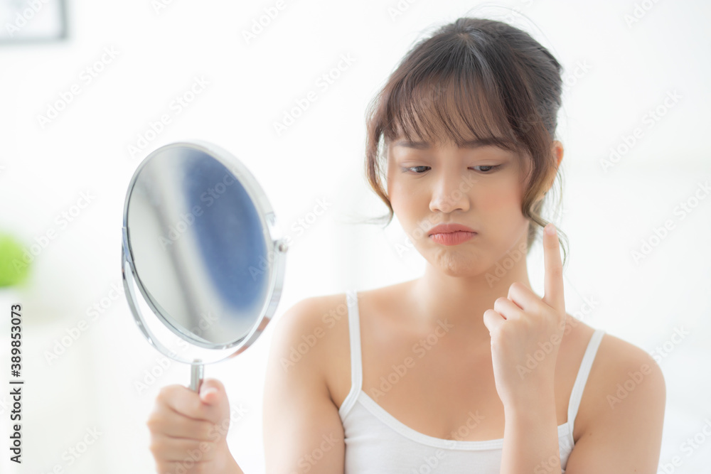 Beautiful young asian woman looking the mirror with acne problem at bedroom, trouble of beauty on face, zit treatment, asia girl is pimple having worry and displeased, skincare and healthy concept. Beautiful young asian woman looking the mirror with acne problem at bedroom, trouble of beauty on face, zit treatment, asia girl is pimple having worry and displeased, skincare and healthy concept.