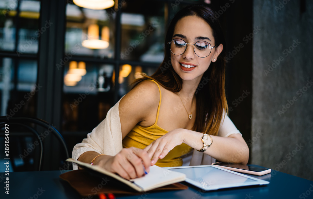 Cheerful young female freelancer taking notes while working in outdoor cafe