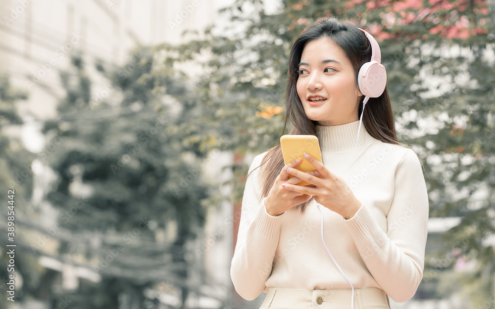 Asian woman chatting on mobile phone, wearing headphone and listening to music
