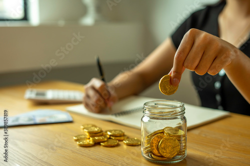 Woman taking note And make income and expenditure accounts by inserting coins in the savings To save money Keep it as retirement money, ideas for saving money for the future