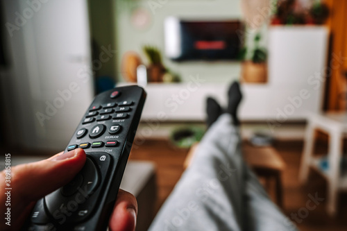 A man is relaxing on the sofa and use the remote control and watch TV in a home with a homely cozy interior