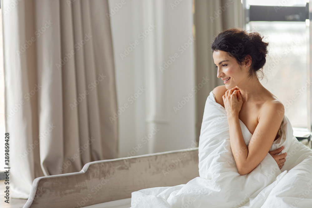 Beautiful charming smiling brunette woman relax in blanket side view. Cozy bedroom with luxury bed. Home or hotel fashion interior. Beautiful charming smiling brunette woman relax in blanket side view. Cozy bedroom with luxury bed. Home or hotel fashion interior.