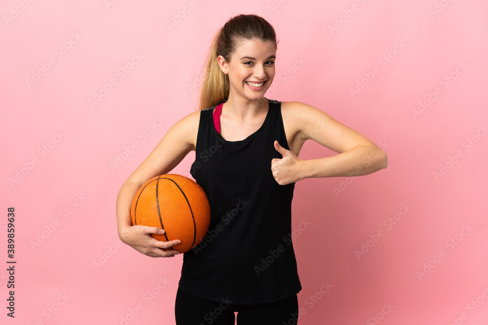 Young blonde woman playing basketball isolated on pink background giving a thumbs up gesture