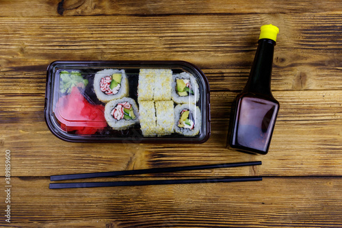 Uramaki sushi rolls with surimi in plastic box on wooden table. Top view. Sushi for take away or delivery of sushi in plastic container