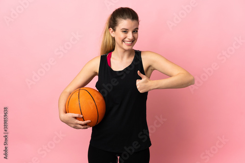 Young blonde woman playing basketball isolated on pink background giving a thumbs up gesture