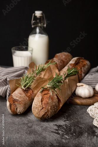 Two wheat baguettes, a glass and a bottle of milk on the table.
