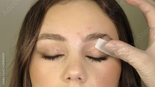 Beautician removes warm wax excess hair from the eyebrow with a special strip. Wax correction of the shape of the eyebrows. Beauty industry close up. Correction of a shape of eyebrows with hot wax