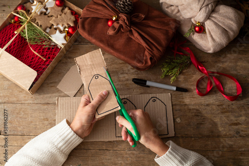 female hands in a white sweater keep eco frindly packed gift with tags from craft cardboard. christmas zero waste concept