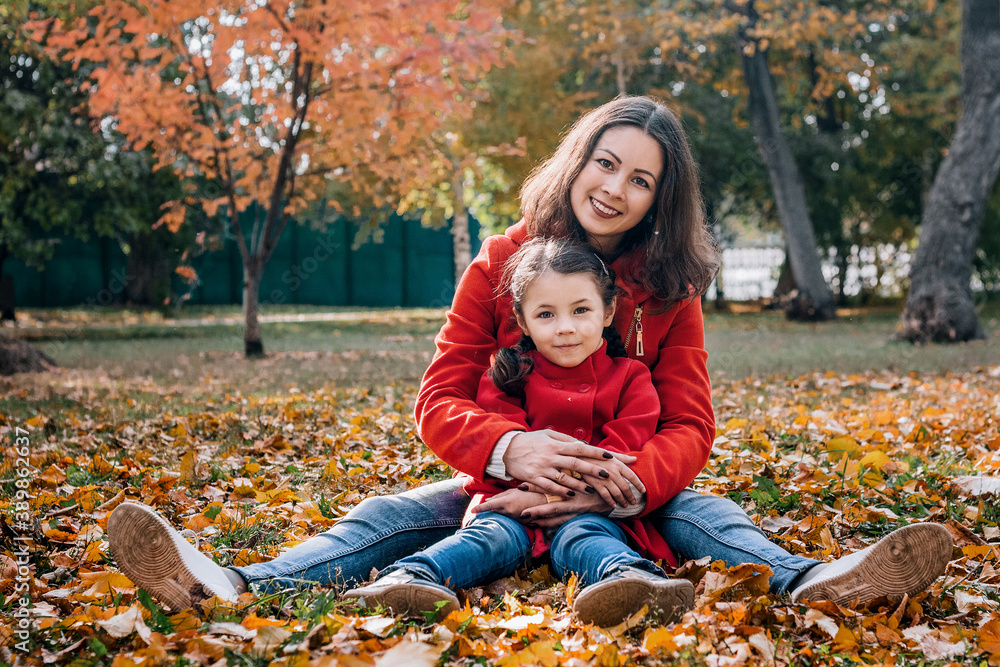 A young mother and her daughter in red coats sit in autumn park A young mother and her daughter in red coats sit in autumn park