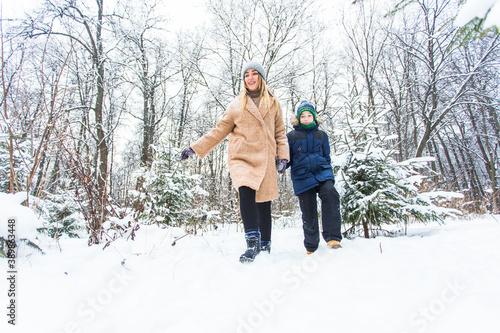 Parenting, fun and season concept - Happy mother and son having fun and playing with snow in winter forest