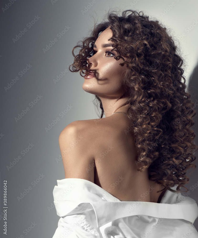 Beautiful young woman with curly hair posing, beauty model portrait,  closeup. Beautiful sexy model girl in white cotton shirt. Flying hair,  perfect make-up and manicure. Hairstyle. Vertical image foto de Stock