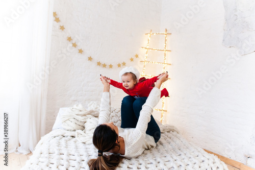 Little caucasian girl in red santa costume playing with her mom on the bed. New year atmosphere.christmas eve