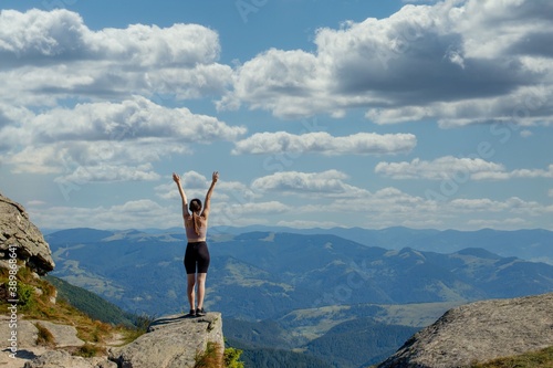 The young Woman at the top of the mountain raised her hands up on blue sky background. The woman climbed to the top and enjoyed her success. Back view