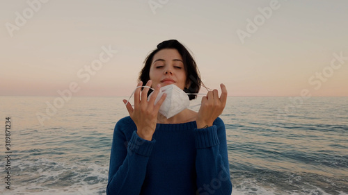Giovane ragazza con maglia blu e mascherina passeggia in riva al mare photo