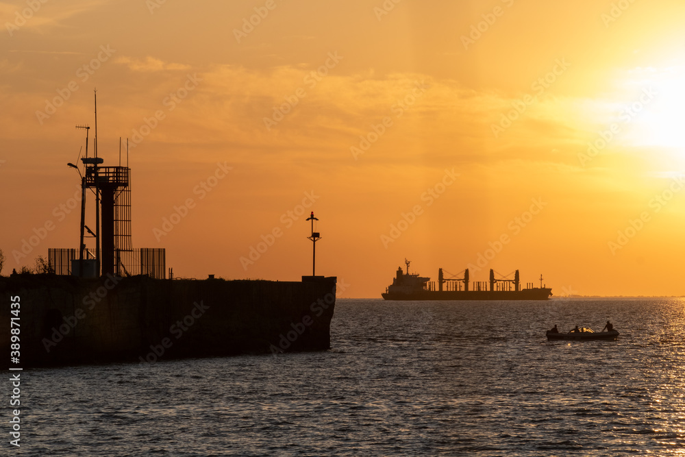 A big cargo ship, a small boat and an old pier can be seen at Uruguay River, Conchillas, Uruguay
