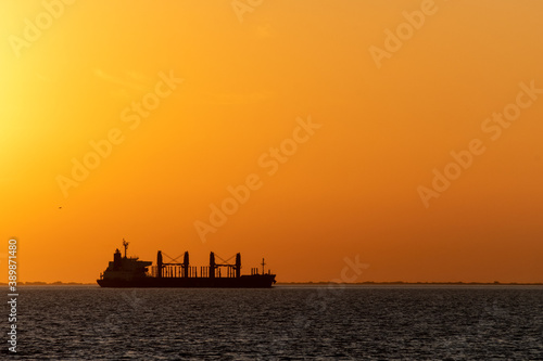 Big cargo ship going through Uruguay river canal at dusk over an orange sky in Conchillas, Colonia, Uruguay. Image with horizontal orientation photo