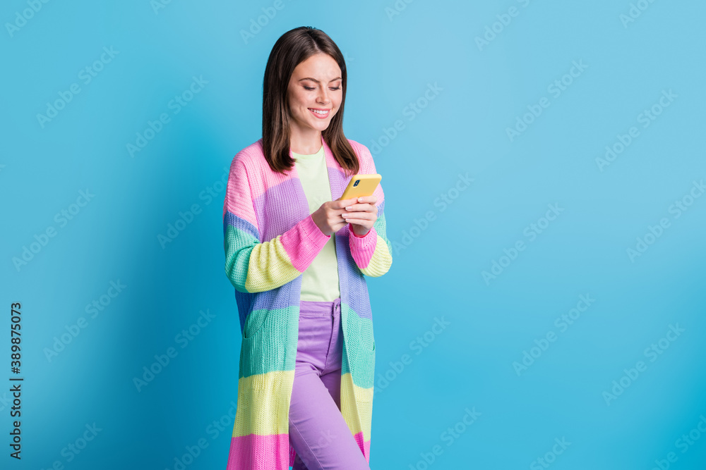 Photo of cheerful brown haired young woman comment post hold hands phone isolated in blue color background Photo of cheerful brown haired young woman comment post hold hands phone isolated in blue color background
