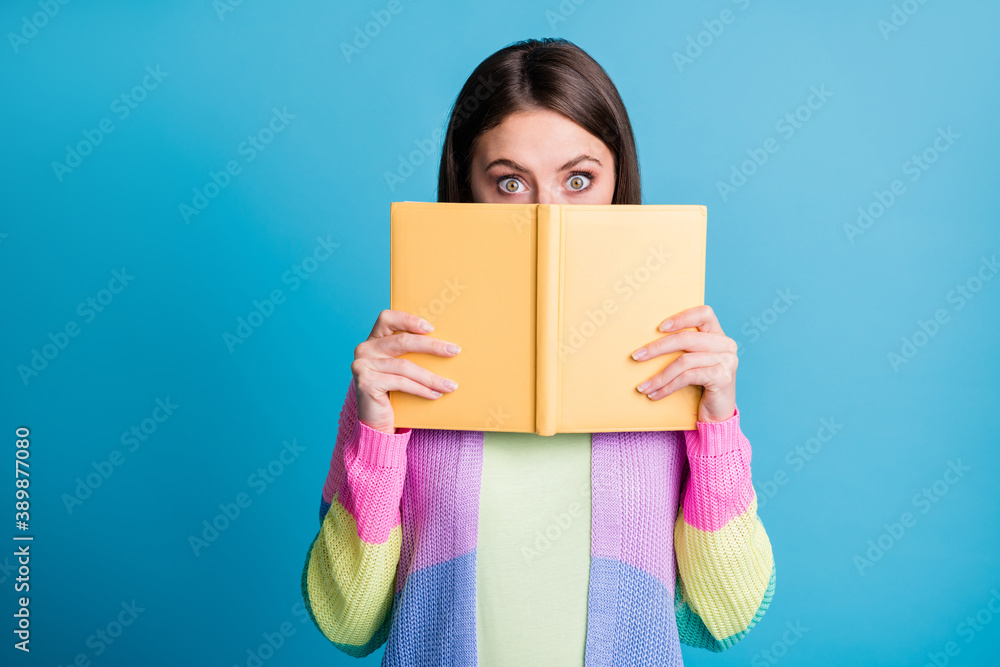 Photo of beautiful brown haired young woman hold copybook cover hide half face isolated blue color background Photo of beautiful brown haired young woman hold copybook cover hide half face isolated blue color background
