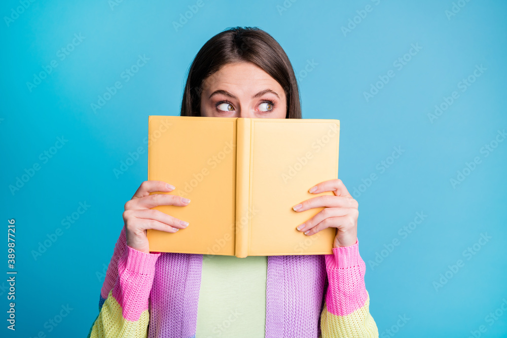 Photo of curious pretty young woman look empty space hold copybook cover face isolated on shine blue color background Photo of curious pretty young woman look empty space hold copybook cover face isolated on shine blue color background