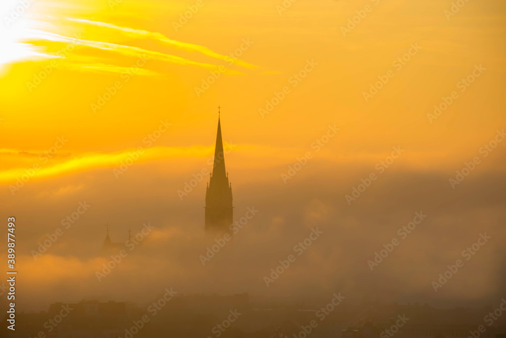 Fototapeta premium Church of the Sacred Heart of Jesus surrounded by fog and clouds, in Graz, Styria region, Austria, at sunrise. Beautiful foggy morning over the city of Graz, in autumn