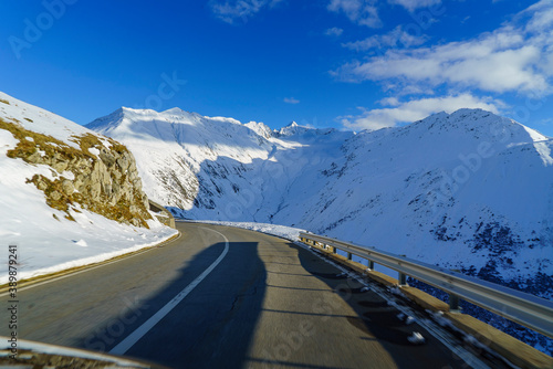 vue depuis une voiture qui roule sur la route d'un col alpin suisse au soleil d'hiver avec des montagnes enneigées tout autour. il n y a pas d autre voiture sur la route