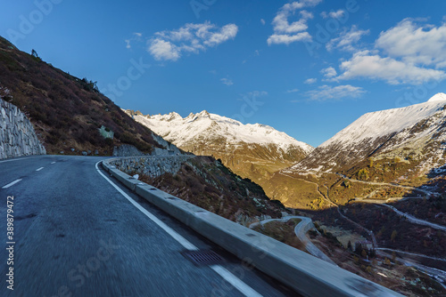 vue depuis une voiture qui roule sur la route d'un col alpin suisse au soleil d'hiver avec des montagnes enneigées tout autour.  il n y a pas d autre voiture sur la route