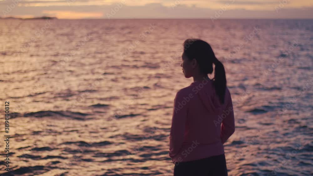 Portrait of a young Asian woman relaxed enjoying peaceful sunset and looking up exhaling fresh air relaxing at the beautiful landscape ocean view.