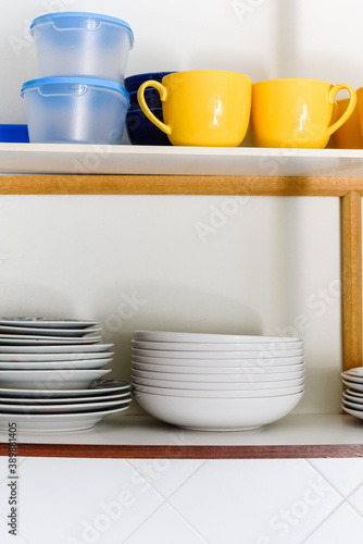 Wooden cupboard with piles of ceramic plates  cups and plastic containers