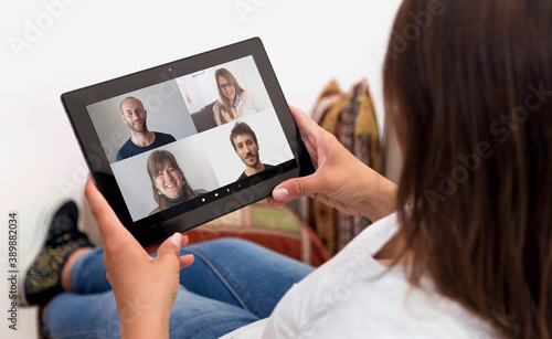 Woman in video conference with a group of people. Girl at home with a tablet in her hands. Young woman resting in a sofa. Millennial girl. Online communications.