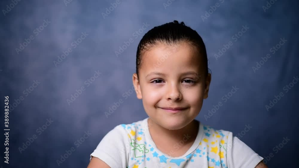 Confident smiling Brazilian girl looking at the camera while standing. Happy laughing. Child with white teeth cute face posing for close up portrait, blue background. Confident smiling Brazilian girl looking at the camera while standing. Happy laughing. Child with white teeth cute face posing for close up portrait, blue background.