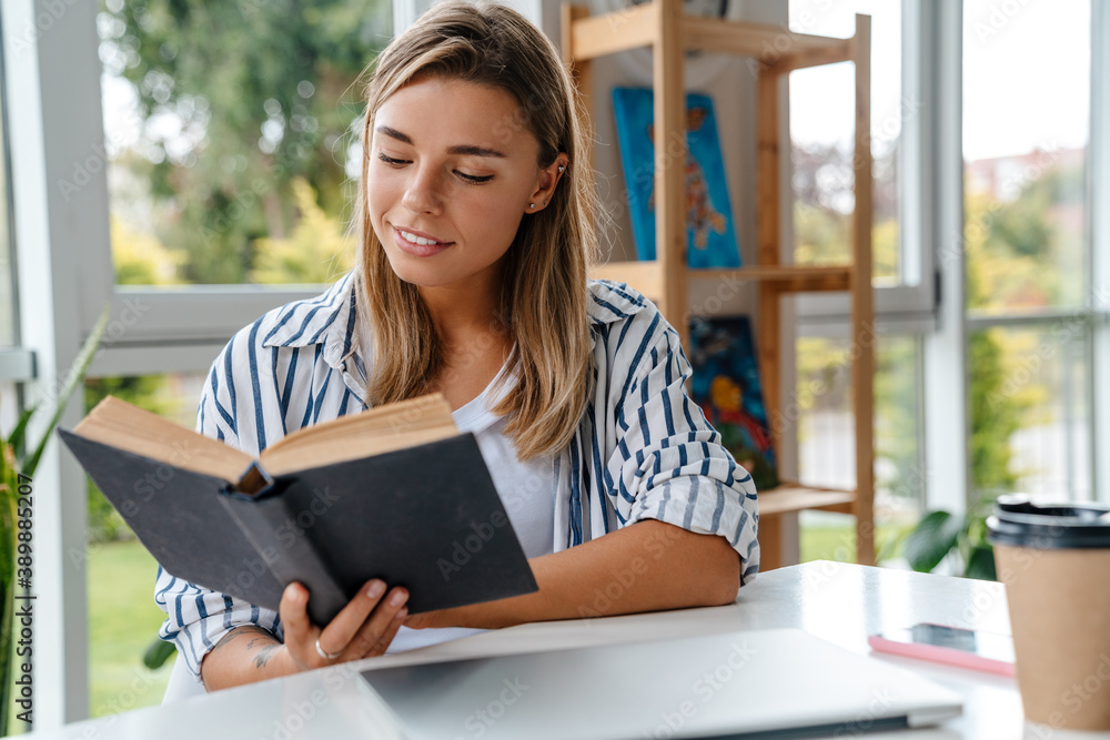 Obraz premium Smiling attractive young woman designer reading book