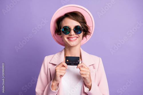 Photo of toothy beaming lady dressed pink retro outfit cap glasses holding credit card arms isolated violet color background © deagreez