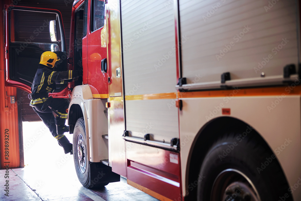 Φωτογραφία Brave firefighter in protective uniform with helmet on head opening door of fire truck and entering in fire station