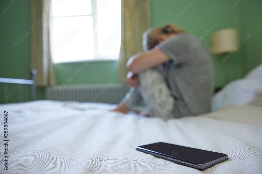 Young Woman In Bedroom Upset By Social Media Trolling And Cyber Bullying On Mobile Phone