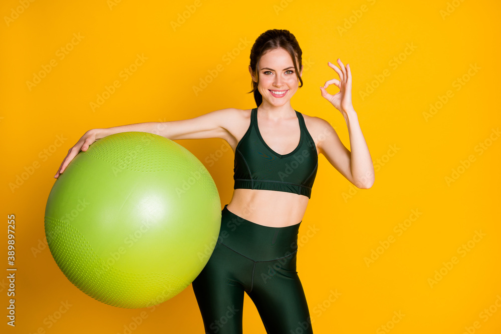 Portrait of attractive content cheery girl holding in hands fitball showing ok-sign advert isolated over bright yellow color background. Portrait of attractive content cheery girl holding in hands fitball showing ok-sign advert isolated over bright yellow color background.