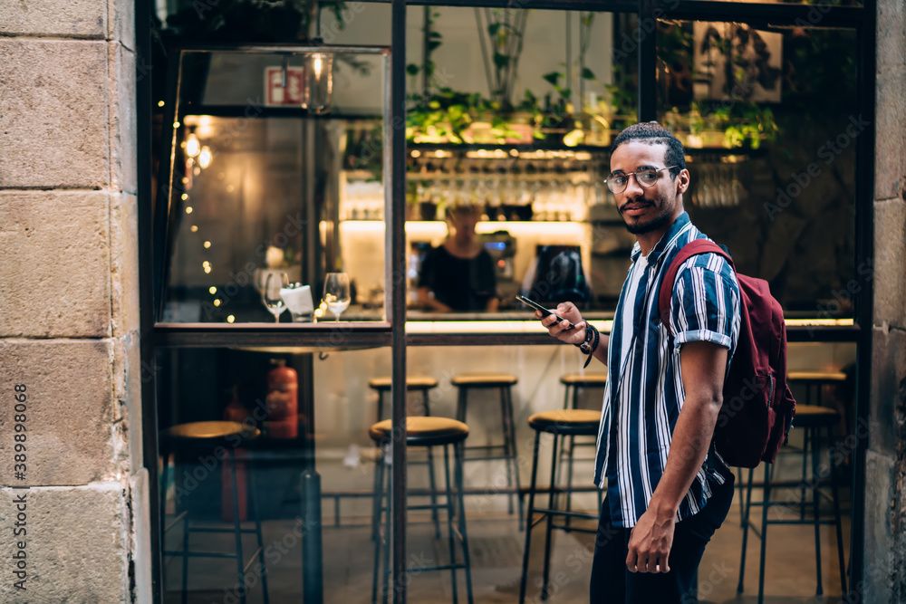 Fototapeta premium Positive ethnic man using smartphone in street cafe