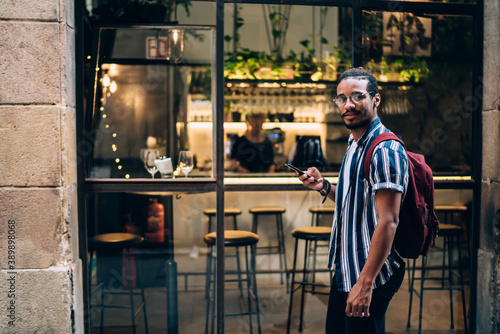 Positive ethnic man using smartphone in street cafe