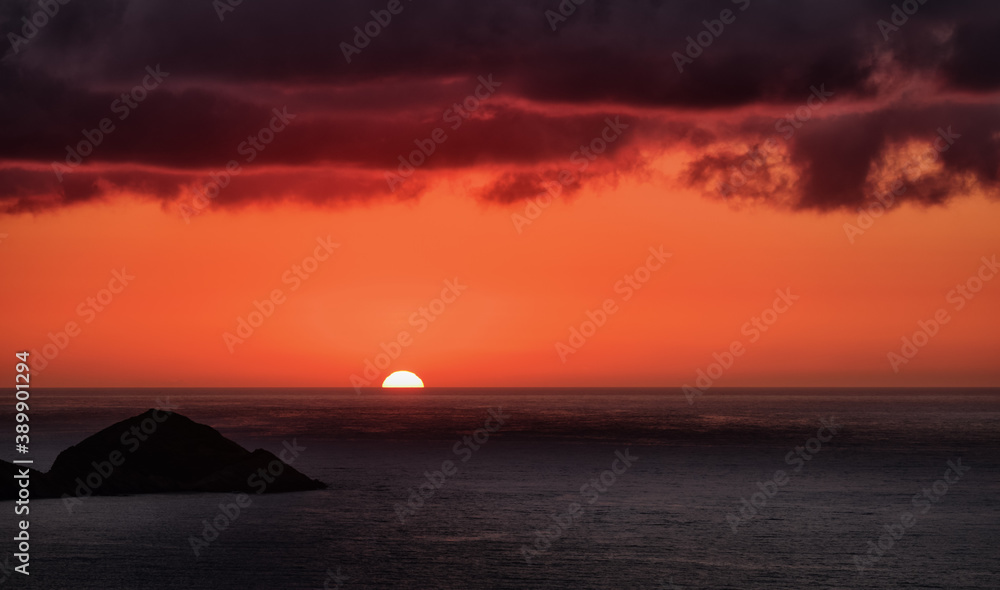 Beautiful sunset in red and purple over sea under heavy stormy clouds. Sun touching horizon.