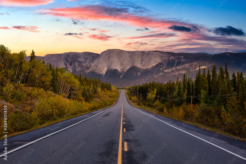 View of Scenic Road surrounded by Trees and Rocky Mountains on a Cloudy Fall Season in Canadian Nature. Colorful Sunset Artistic Render. Taken near Whitehorse, Yukon, Canada.