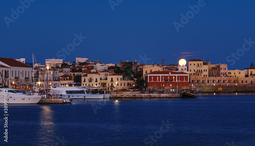 Full moon setting over Chania s Old Venetian Harbour. Night view of piers  boats and Maritime museum of Crete and houses over marina.