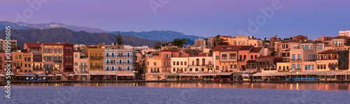 Sunrise or sunset over Old Venetian port and harbour promenade of Chania, Crete, Greece. Great purple sky, distant Cretan mountains. Panoramic shot.