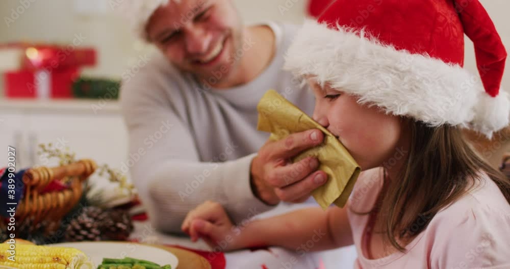 Caucasian senior man in santa hat wiping his daughter face with tissue sitting on dining table and e Caucasian senior man in santa hat wiping his daughter face with tissue sitting on dining table and e