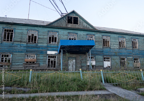 A wooden house with Windows behind a fence stands at a fork in the road . wooden houses in the city of Batagay. Yakutia. Russia.