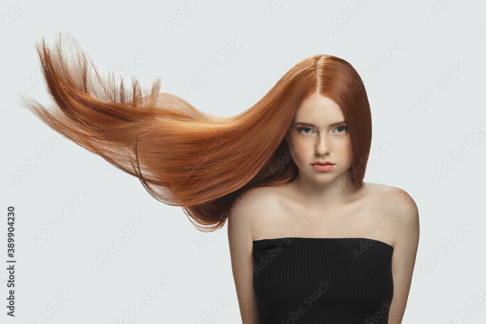 Silk. Beautiful model with long smooth, flying red hair isolated on white  studio background. Young girl with well-kept skin and hair blowing on air.  Concept of salon care, beauty, fashion. Stock Photo