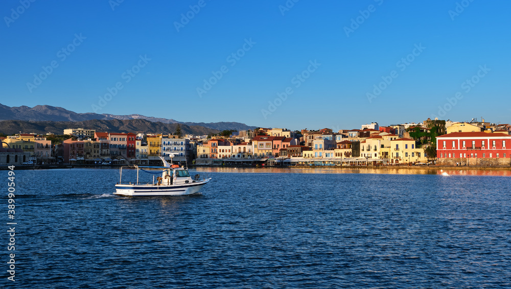 White fishing boat passing by Old Venetian harbour quay and Maritime museum in Chania, Crete, Greece. Cretan hills and mountains. Early morning.