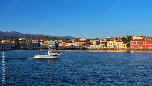 White fishing boat passing by Old Venetian harbour quay and Maritime museum in Chania  Crete  Greece. Cretan hills and mountains. Early morning.