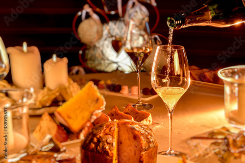 champagne is poured into glass on table set in Christmas style with blurred panettone and candles, warm mood light