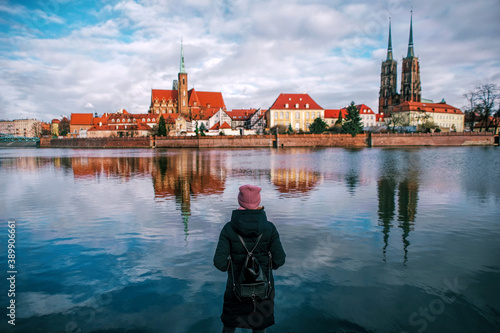 Woman in winter clothes looks at a european city center across the lake. Rear view of Woman looking at city with red roof, evening view