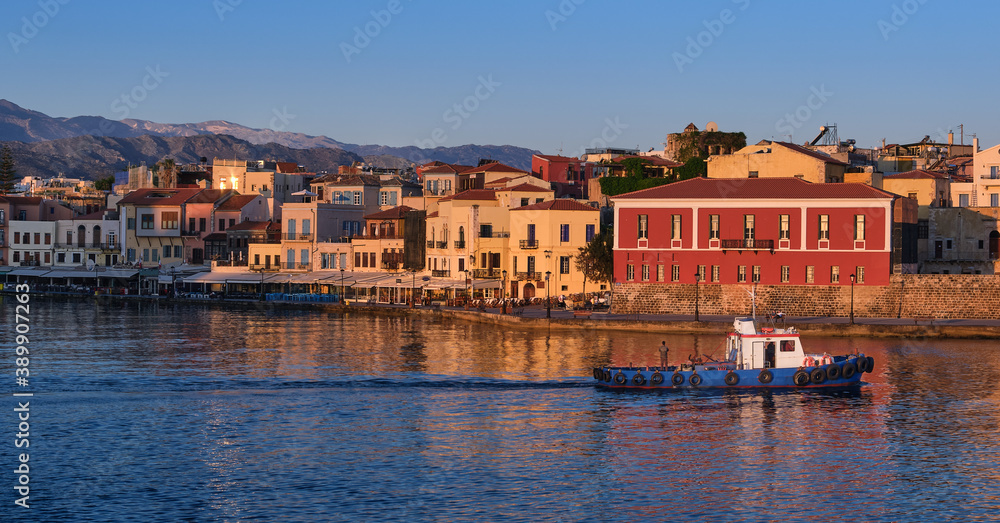 Fishing boat pass by Old Venetian harbour quay, Maritime museum of Crete in Chania, Crete, Greece. Sunrise, Cretan hills and mountains. First sun rays